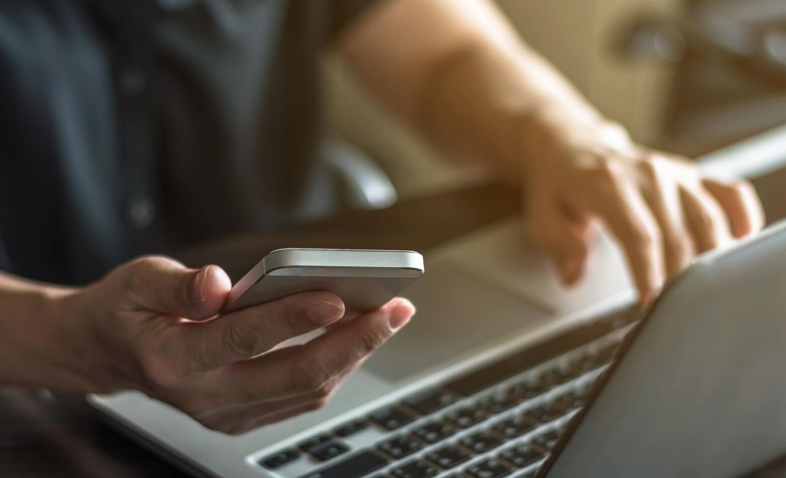 Close-up of a person multitasking on a laptop and smartphone in a work setting – Neutrinos