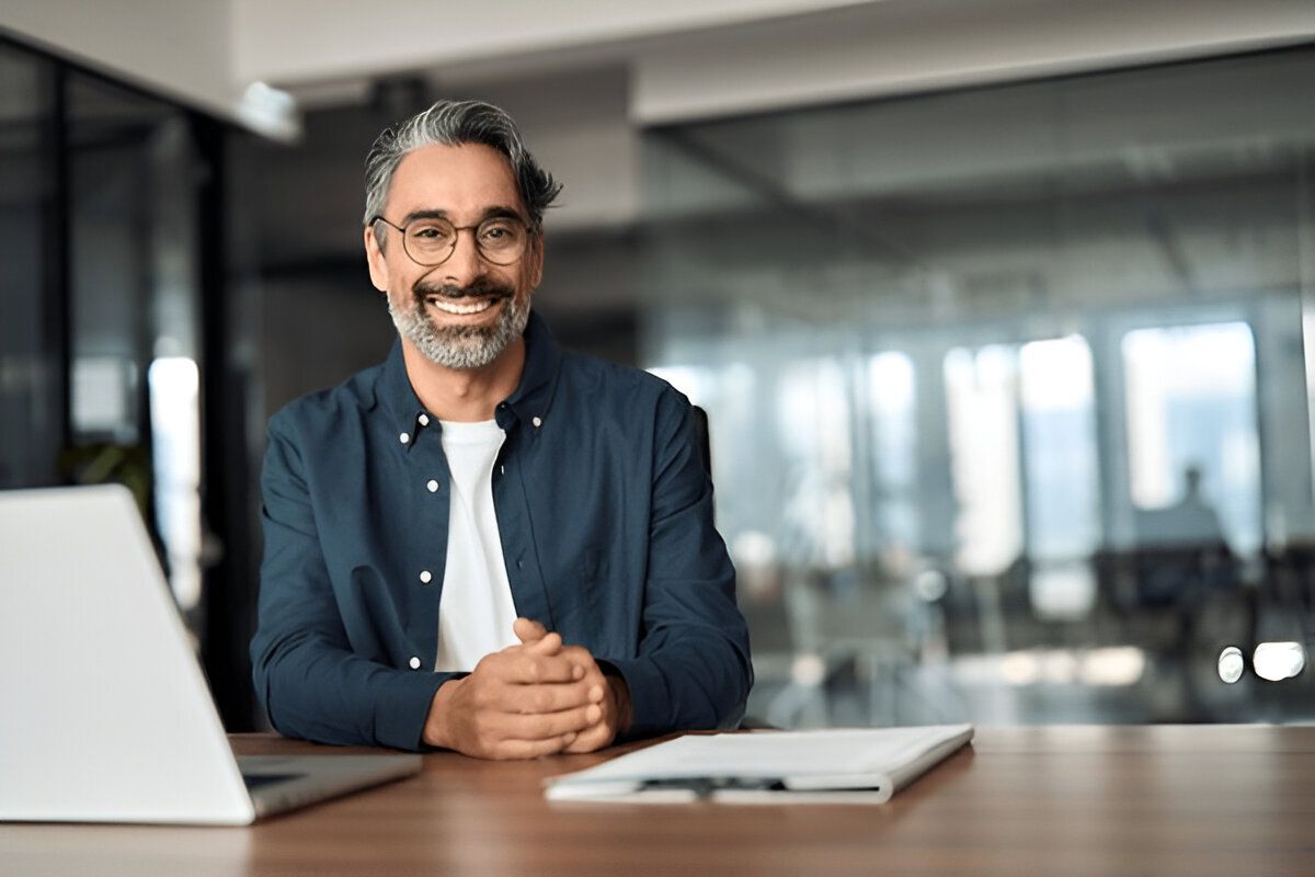 Confident business leader smiling at desk with laptop and notes – Neutrinos