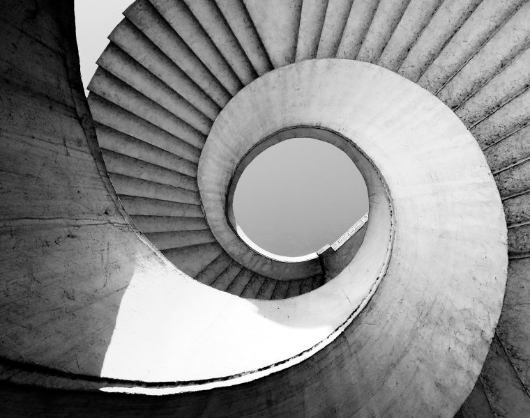 Black and white view of a spiral concrete staircase with a circular opening at the top-Neutrinos