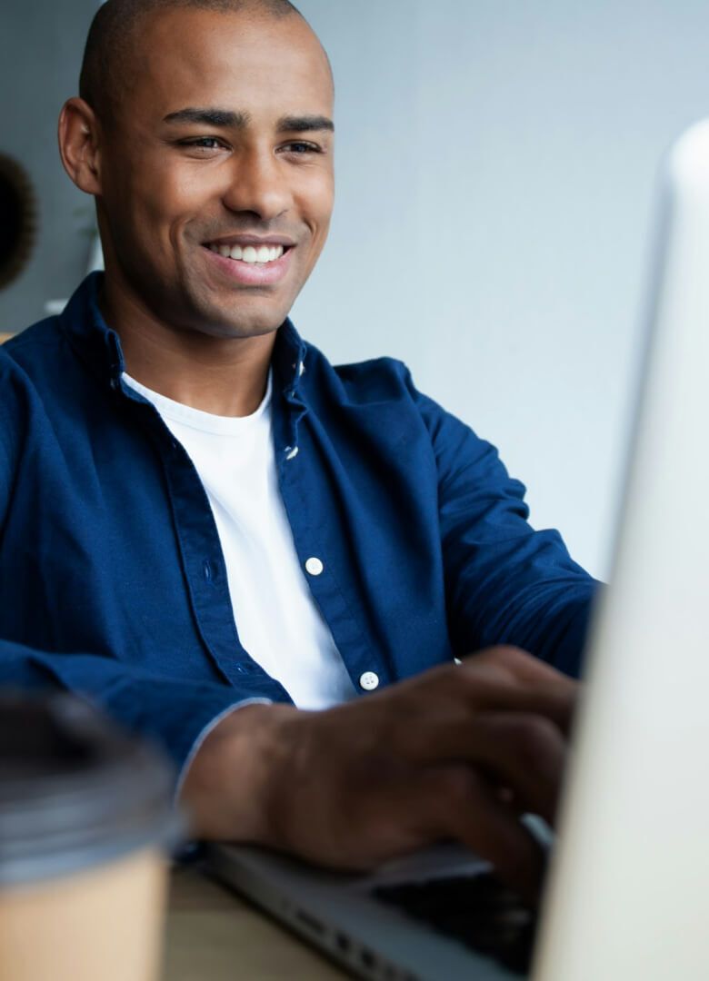 Young professional man smiling while working on laptop at desk with coffee cup - Neutrinos